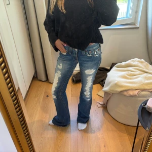 Blå bootcut jeans med slitningar - Säljer ett par blå bootcut jeans med kraftiga slitningar och destroyed detaljer framtill. Jeansen har låg midja och klassiska fem fickor. Materialet är denim och passformen är loose med utsvängda ben. Perfekta för en avslappnad och trendig look. Köpta secondhand i Danmark 😇xs/s