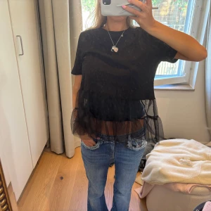 Svart blus med volang och mesh - Supersnygg svart blus med kort ärm och transparent meshvolang nertill. Toppen har en rak passform och coola lager av tyll som ger en trendig look. Perfekt att styla med jeans för en chill men ändå unik outfit.