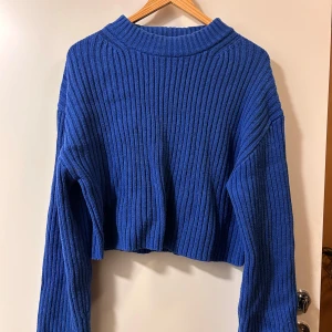 Blå ribbad croppad stickad tröja - Säljer en blå croppad stickad tröja med ribbat mönster och lång ärm. Tröjan har en högre halsringning och är perfekt för dig som gillar en chill och trendig stil. Passformen är loose och den är superenkel att matcha med jeans eller kjol.