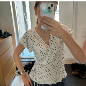 Vit omlottblus med svarta prickar - Söt vit omlottblus med svarta prickar och knyt i midjan. Blusen har korta, lite fladdriga ärmar och v-ringning. Storlek M men sitter som S💕💕