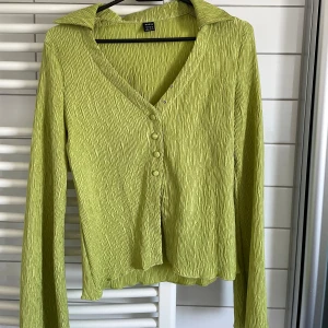 Grön crinkle kofta  - Snygg ljusgrön kofta med crinkle-effekt i tyget. Modellen har v-ringning, krage och knappar framtill. 