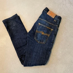 Mörkblå skinny jeans från Nudie - Snygga mörkblå jeans från Nudie Jeans i ekologisk bomull. Klassisk femficksmodell med orangea kontrastsömmar och Nudie-logga på bakfickan. Jeansen har en smal passform och raka ben, perfekt för en clean och stilren look.