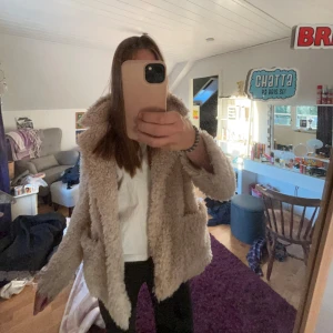 Beige teddyjacka med stora fickor - Supermysig beige teddyjacka med fluffigt material och stora fickor framtill. Jackan har en bred krage och är långärmad, perfekt för kyliga dagar. Passformen är lite loose och den är enkel att slänga på sig över vilken outfit som helst.