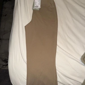 Beiga slim kostymbyxor XS - Snygga beiga kostymbyxor i slim fit med hög midja. Byxorna har en stilren look utan synliga fickor eller detaljer och är gjorda i ett mjukt, stretchigt material som sitter skönt. Perfekta för en clean och modern stil.