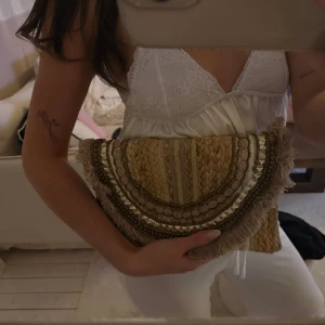 Clutch  - Säljer en superfin kuvertväska i beige med flätad struktur och snygga detaljer som pärlor, guldiga paljetter och fransar längs kanten. Inköpt på en marknad i Cannes och i superfint skick 🩷