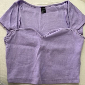 Ljuslila croppad topp från SHEIN - Trendig ljuslila croppad topp från SHEIN med korta ärmar och snygg v-ringad detalj framtill. Toppen är ribbad och har en figurnära passform som ger en modern look. Perfekt att matcha med jeans eller kjol för en cool stil.