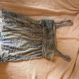 Babydoll topp med djurmönster - Säljer en topp med tunna axelband och coolt djurmönster i beige, grå och bruna toner. Toppen har ett flowigt tyg och är perfekt för dig som gillar unika prints och en avslappnad stil. Passar dig som vill sticka ut med ett vilt mönster.