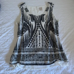 Svartvit mönstrad linnetopp Carla F. - Snygg ärmlös linnetopp från Carla F. i vitt med svart grafiskt mönster framtill. Toppen har rund halsringning och lätt utsvängd passform. Perfekt för dig som gillar unika prints och vill ha en luftig topp till sommaren.