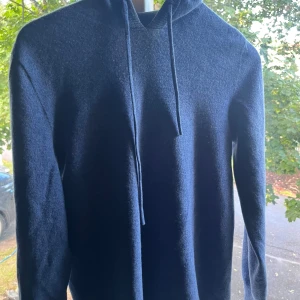 Ljusblå Kashmir hoodie - Säljer en ljusblå hoodie med huva och snörning. Tröjan är stickad i material kasmir och har långa ärmar samt ribbade muddar vid hals och ärmslut. Perfekt för dig som gillar en enkel och stilren look med lite extra mysfaktor.