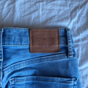Levi's ljusblå skinny jeans - Snygga ljusblå jeans från Levi's med klassisk röd logotag vid bakfickan och brunt läderpatch i midjan. Modellen har smal passform och raka ben, med fem fickor och knappgylf. Perfekta för dig som gillar en clean och tidlös look.