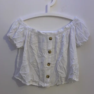 Vit offshoulder blus från H&M - Supersöt vit blus från H&M i offshoulder-modell med korta puffärmar och snygga knappar framtill. Gjord i ett lätt, krinklat bomullstyg som känns luftigt och fräscht. Pris kan diskuteras!
