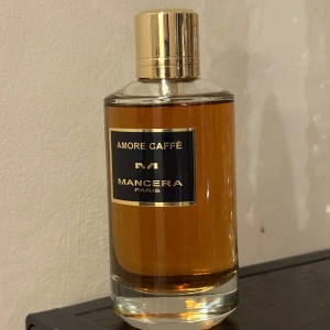 Mancera Amore Caffè parfym - Lyxig parfym från Mancera, Amore Caffè, i en elegant cylindrisk glasflaska med guldigt lock och svart etikett med gulddetaljer. Doften har en varm bärnstensfärgad vätska som ger exklusiv känsla.