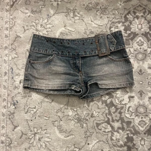 MOTO jeansshorts med bredt bälte - Snygga mörkblå jeansshorts från MOTO med  låg midja och stort bälte med metallspänne. Shortsen har slitna detaljer, klassiska fickor fram och bak samt coola sömmar på bakfickorna. Perfekta för sommaren och ger en edgy vibe.