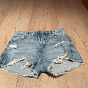 Blå jeansshorts med slitningar - Snygga blå jeansshorts med slitningar och fransiga kanter. Säljer för jag tyverr växt ur dom, shortsen är i storlek xs💕💕