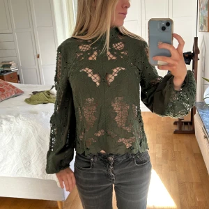 Grön spetsblus - Säljer en elegant grön spetsblus med långa ärmar och vackra blommiga detaljer. Blusen har en hög hals och är perfekt för en stilfull look. 
