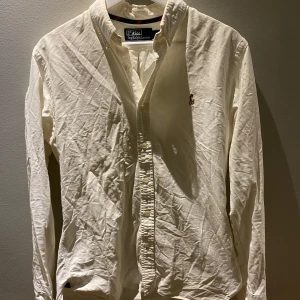 Vit skjorta från Polo Ralph Lauren - Säljer en klassisk vit skjorta från Polo Ralph Lauren i slim fit. Skjortan har långa ärmar och en broderad logotyp på bröstet. Perfekt för en stilren look.