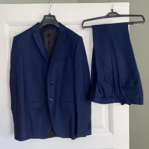 Mörkblå kostym från Jack & Jones Premium - Säljer en elegant mörkblå kostym från Jack & Jones i slim passform. Kostymen består av en kavaj och matchande byxor, perfekt för formella tillfällen. Använd endast en gång på min skolbal så mycket bra skick. Galgar och kostymväska ingår. STORLEK 46 i båda, vilket passar typ xs eller litet s. Nypris 2499. 