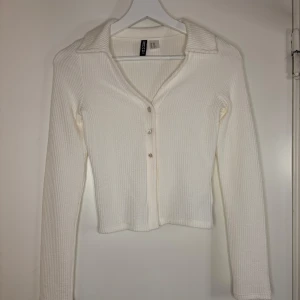 Vit ribbad kofta/tröja - Säljer en vit ribbad kofta med knappar framtill. Den har en klassisk krage och långa ärmar. Passar både till vardag och mer uppklädda tillfällen. Endast använd en gång då jag fått den och sedan tyckte att den va lite liten, enligt min smak. 