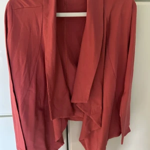 Röd cardigan jacka från Icona - Säljer en snygg röd cardigan jacka från Icona. Jackan är tillverkad i en mjuk bomullsblandning med elastan för extra komfort. Den har en öppen design utan knappar och långa ärmar. Rostfärgad Oanvänd 