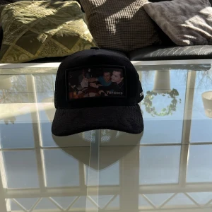 Svart keps från Tophood - Snygg svart keps från Tophood med ett unikt tryck framtill. Kepsen har ett nätmaterial baktill för bättre ventilation och justerbar rem för perfekt passform. Perfekt för en avslappnad stil.