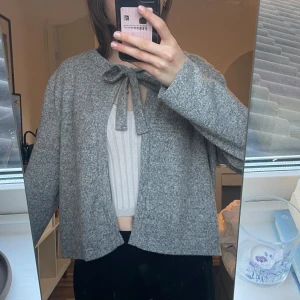 Grå cardigan jacka med knyt - Säljer en stilren grå cardigan jacka med knyt framtill. Jackan har en lös passform och långa ärmar, perfekt för en avslappnad look. Den är tillverkad i ett mjukt material som ger en bekväm känsla.