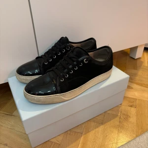 Svarta sneakers från Lanvin - Snygga svarta sneakers från Lanvin med glansig tå och snörning. Skorna har en vit sula som ger en fin kontrast till det svarta. Perfekta för en stilren look. Digitalt kvitto finns, pris kan diskuteras!
