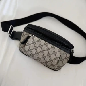 Mönstrad magväska  - Säljer en snygg magväska med klassiskt mönster i beige och svart. Väskan har en justerbar rem och flera dragkedjafack. För smidig förvaring. Perfekt för att hålla dina saker säkra och nära till hands.