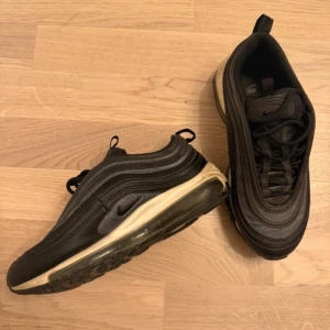 Svarta Nike Air Max 97 - Säljer ett par svarta Nike Air Max 97 med den ikoniska vågdesignen och synlig Air-enhet i sulan. Skorna har en stilren look med snörning och en bekväm passform. Perfekta för både vardag och träning. Glitter !  
