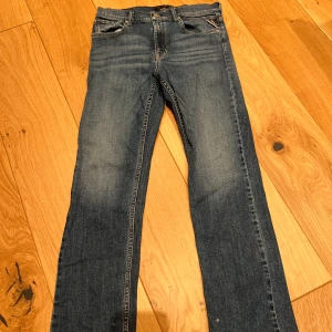 Blå jeans från Replay - Snygga blå jeans från Replay med klassisk femficksdesign och lätt slitna detaljer. De har en normal passform och är perfekta för en avslappnad stil. Märkeslogga på baksidan och knappgylf framtill.