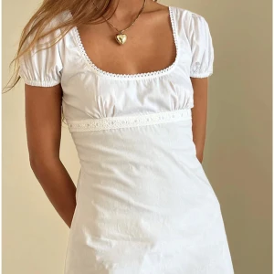 Vit mini klänning från Motelrocks - Säljer en söt vit klänning från Motelrocks med kort puffärm och volangdetaljer. Aldrig använd med lappen kvar. Storlek xxs, passar mig som är 158cm. Klänningen har en fyrkantig urringning och spetsdetaljer vid midjan och fållen. Perfekt för sommaren, student eller liknande!