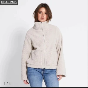 Beige teddyjacka med dragkedja - Mysig beige teddyjacka med dragkedja framtill. Jackan har en hög krage och långa ärmar, perfekt för kyliga dagar. Den har en avslappnad passform och är gjord i ett mjukt teddy-material.