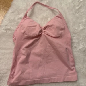 Rosa halternecklinne - Säljer ett sött rosa halternecklinne med knytband runt nacken. Linnet har en enkel design med en lätt rynkad detalj framtill. Perfekt för träning !