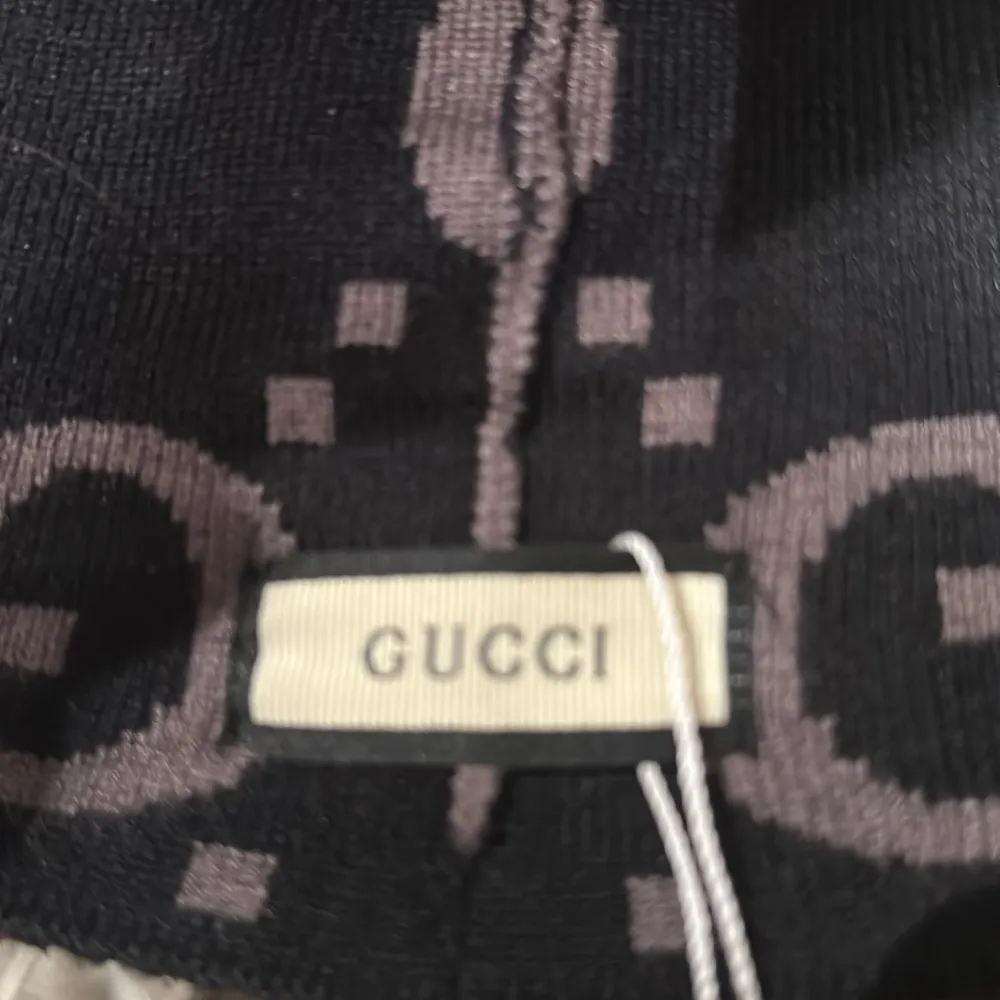Snygg svart och grå mössa från Gucci med det ikoniska GG-mönstret. Mössan har en ribbad kant i svart och grått som ger en stilren look. Perfekt för att hålla sig varm med stil.. Asusteet.