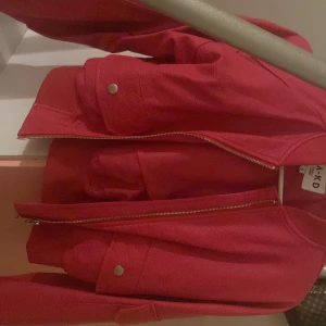 Röd bomberjacka från NA-KD - Säljer en snygg röd bomberjacka från NA-KD. Jackan har dragkedja framtill och praktiska fickor med knappar. Perfekt för att ge din outfit en färgklick! Har använts ett flertal gånger men ny tvättad och har inga skador.