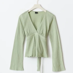 Grön v-ringad topp från gina  - Snygg grön v-ringad topp från gina med långa ärmar och knytband i midjan. Perfekt för en stilren look. Den är M men passar s