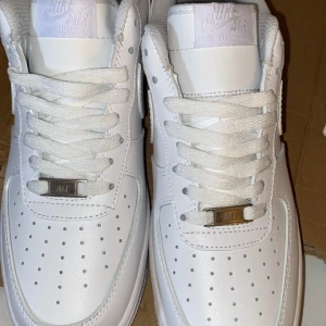 Vita Nike Air Force 1 - Säljer ett par klassiska vita Nike Air Force 1 med snygg snörning och perforerade detaljer på tån. Skorna har en stilren design med Nike-logga på hälen och tungan. Pris går att diskutera 