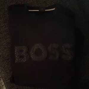 Svart tröja från Boss - Säljer en stilren svart tröja från Boss. Tröjan är inte använd alls mycket och säljer den nu för att den inte passar min stil