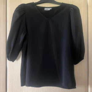 Svart blus med v-ringning - Elegant svart blus med v-ringning och trekvartsärmar. Perfekt för en stilren look.