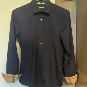 Mörkblå burberry skjorta - Snygg mörkblå skjorta från Burberry. Skjortan är i storlek xs. Skjortan är i bra skick och har inga synliga defekter. Tveka inte på att höra av dig för fler frågor eller funderingar!