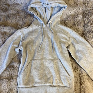 Grå hoodie från NA-KD - Hoodie från NA-KD i storlek XS. Den har en klassisk design med en stor ficka framtill och justerbar huva. Perfekt för en avslappnad look.