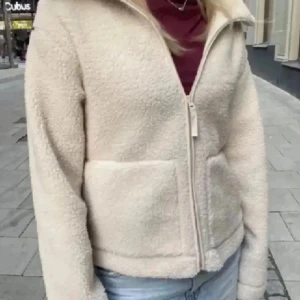 Beige teddyjacka H&M - Mysig beige teddyjacka med dragkedja framtill och hög krage. Jackan har långa ärmar och två praktiska fickor. Perfekt för kyliga dagar när du vill hålla dig varm och bekväm.