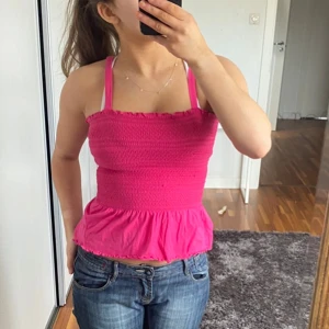 Rosa smockad tubtopp - Säljer en söt rosa smockad tubtopp med volangdetalj i nederkant. Toppen har avtagbara axelband och en elastisk passform som gör den bekväm att bära. Perfekt för sommardagar! 🌸