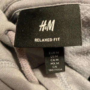 Grå hoodie från H&M - Säljer en grå hoodie från H&M i relaxed fit. Den har en klassisk design med en stor ficka framtill och justerbar huva. Perfekt för en avslappnad stil.