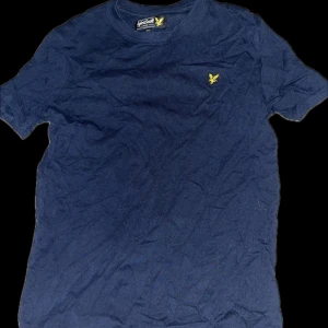 Mörkblå t-shirt från Lyle & Scott - Säljer en stilren mörkblå t-shirt från Lyle & Scott med deras ikoniska gula logga på bröstet. Perfekt för en avslappnad look. Passar bra till jeans eller shorts.