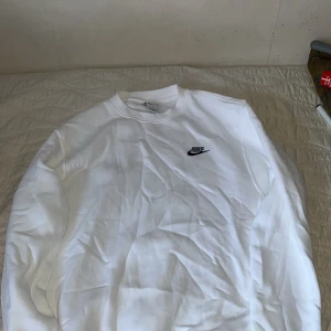 Vit sweatshirt från Nike - Säljer en klassisk vit sweatshirt från Nike med deras ikoniska logga på bröstet. Tröjan har en rund hals och långa ärmar, perfekt för en avslappnad stil. Passar bra till både jeans och träningsbyxor.