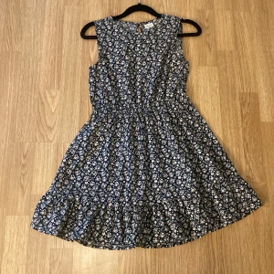 Blommig ärmlös klänning från basic needs by nameit - Supersöt ärmlös klänning från basic needs by nameit i marinblått med små vita och ljusrosa blommor. Klänningen har resår i midjan och volang nertill för en extra fin touch. Perfekt för varma dagar och somriga tillfällen. Resåren går inte att spänna åt men det går att knyta åt som en fin detalj runt midjan :) 