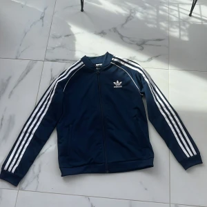 Blå adidas zip up hoodie - Jättefin ”hoodie” från adidas! Jag har tyvärr växt ur den så behöver sälja🥲Jag har själv använt den, men skicket på den är superfint. Det står inte vilken storlek, men jag är 158 cm och den är lite för liten, skulle uppskatta att den är ca 152-158. 🫶🏻💕Pris kan diskuteras! Nypris 599 