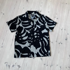 Skjorta - Kortärmad skjorta från H&M i regular fit med svart och vitt bladmönster. Skjortan har knappar framtill och klassisk krage. Perfekt för dig som vill sticka ut med en cool och modern stil. Hör av dig vid minsta fundering!🔥💥