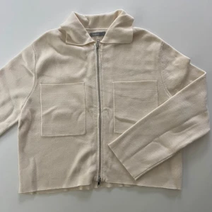 Beige cardigan jacka med dragkedja - Säljer en stilren beige cardigan jacka med dragkedja framtill och två stora fickor på bröstet. Jackan har lång ärm och en mjuk, lätt struktur. Perfekt för lager-på-lager och enkel att matcha.