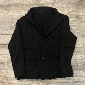 Svart kavajkofta från John Henric - Stilren svart kavajkofta från John Henric med klassisk krage och två knappar framtill. Koftan har fickor på sidorna och en bröstficka. Perfekt för en dressad look och enkel att matcha med olika outfits. | Skick 7/10. Den är lite urtvättad vilket gör att den har krympt lite | Pris 429kr inte hugget i sten | Hör av dig vid fler frågor!